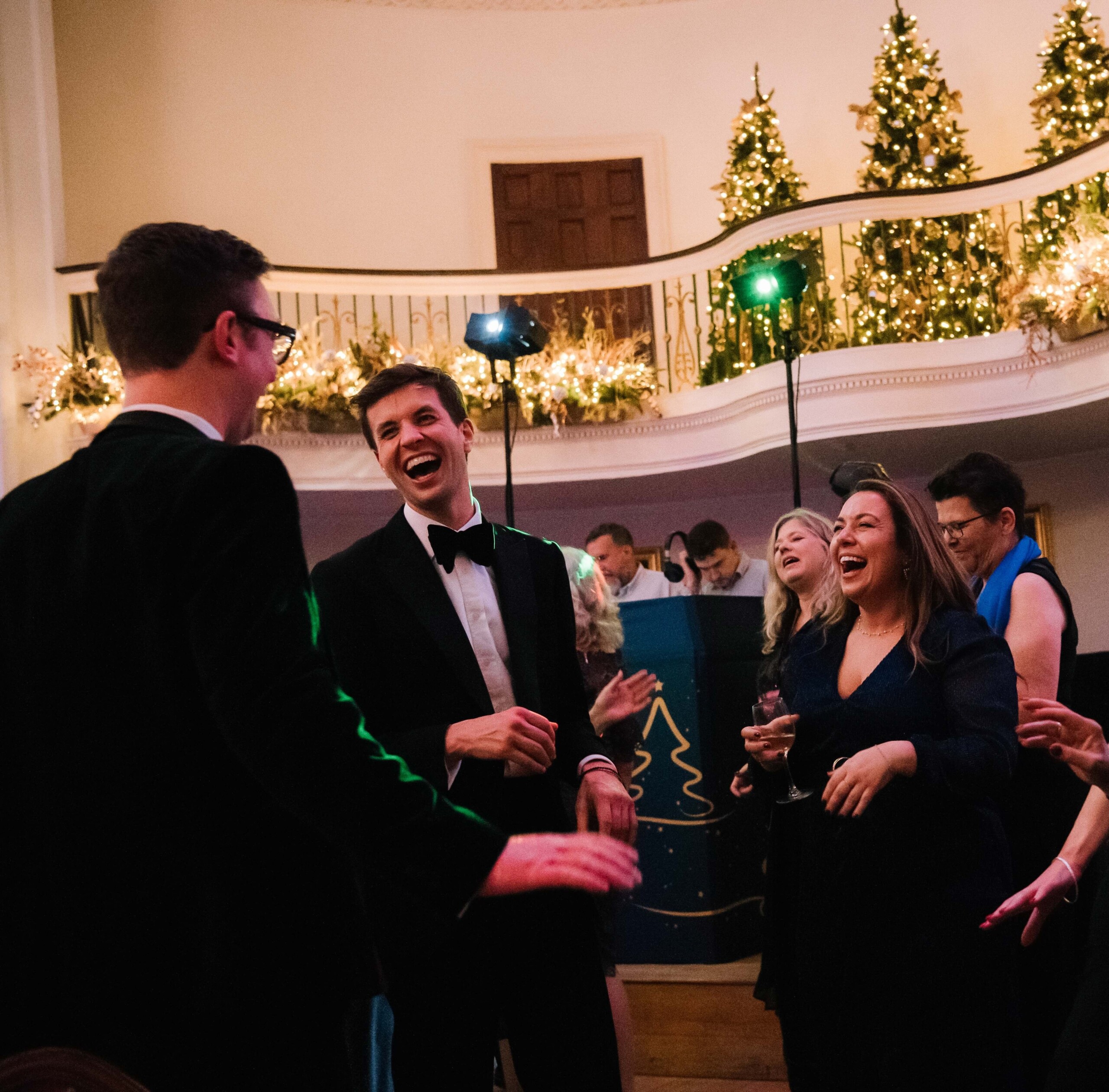 Friends and colleagues dance underneath the Pump Room balcony, bedecked with Christmas trees